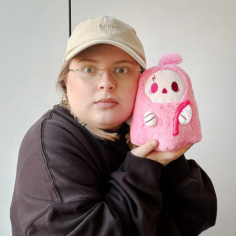 Image shows a woman holding up the pink stuffed reaper. It is slightly smaller than her head.