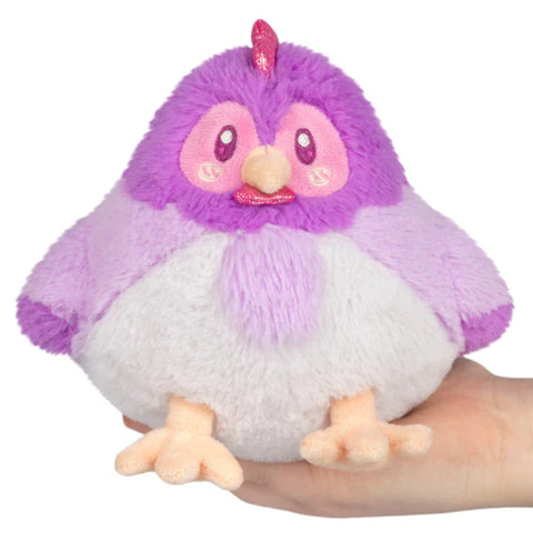 Plush purple hen held in an adult's palm on a white background