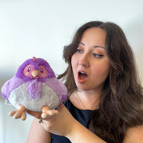 Woman holding the plush purple hen toy. It is slightly smaller than her head.