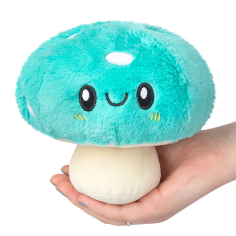 A plush toy resembling a turquoise mushroom with a smiling face, being held in a person's hand.