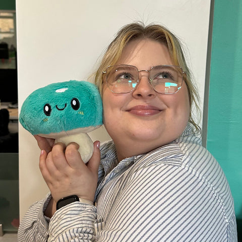 A woman holds the plush mushroom near her face. It is slightly smaller than her head.