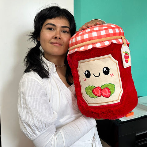 A woman holds the plush strawberry jam. It is about the size of her torso.