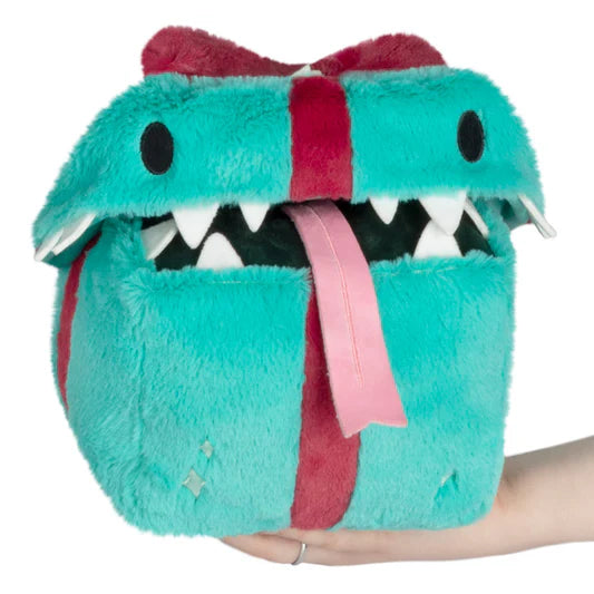 A stuffed turquoise gift with a red bow. The gift has eyes and is open at the lid with teeth and a tongue sticking out