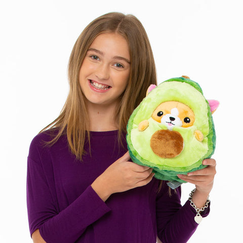 Image shows a teenage girl holding up the avocado corgi. It is slightly larger than her head.