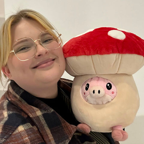 A woman holds the pig in the mushroom suit near her face. It is slightly larger than her head.