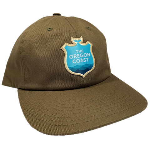 Image shows an olive green trucker hat with a patch. The patch is blue, reads "The Oregon Coast", and has waves.