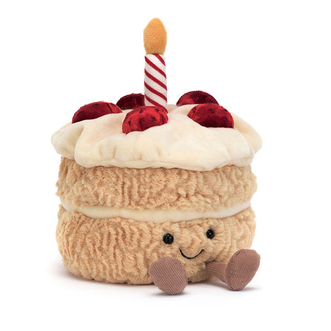 Image shows a stuffed vanilla layer cake with berries and a candle on top. It has a happy face and feet.