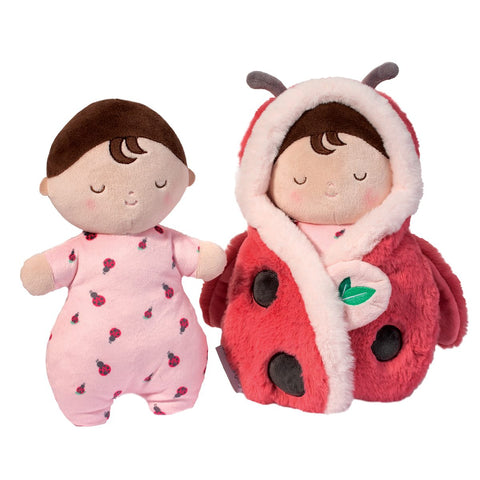 A plush doll next to the same doll wrapped in a ladybug blanket. The doll has pale skin, brown hair, and is wearing a strawberry onesie.