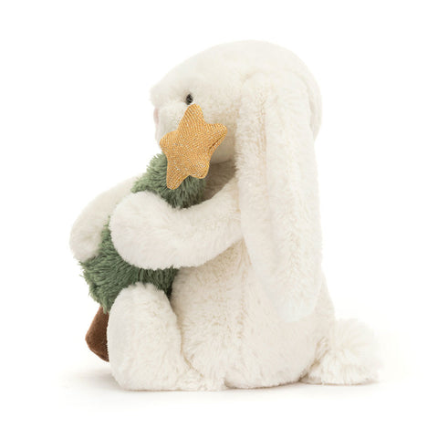 Side view of a plush white bunny toy holding a Christmas tree