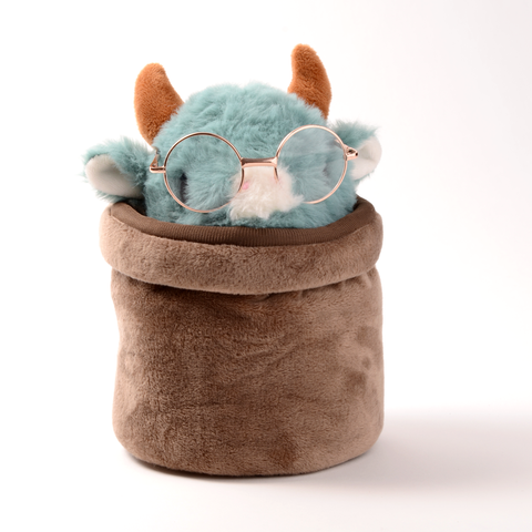 A plush stuffed animal resembling a cow with blue fur, wearing glasses and sitting in a brown plush pot.