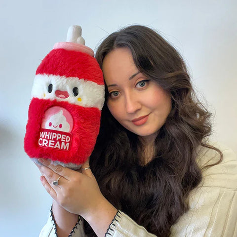 A woman holds the plush whipped cream can near her face. It is slightly larger than her head.