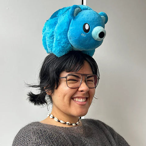 A woman wearing the blue plush tardigrade on her head. It is slightly larger than her head.