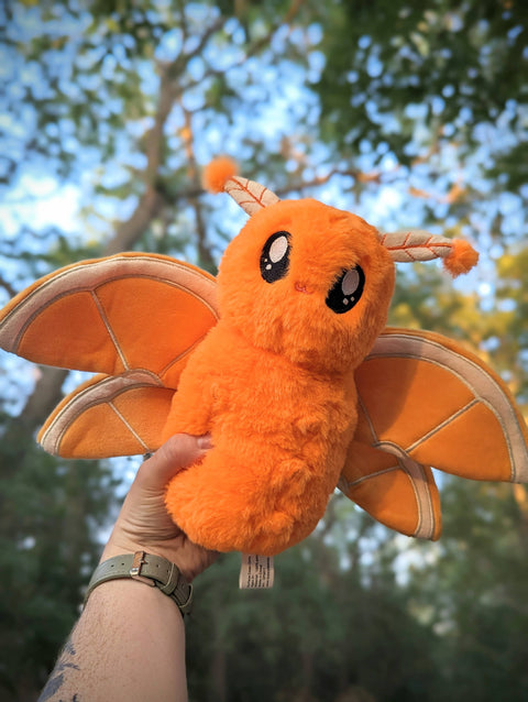 Image shows a stuffed orange fruit themed moth. It is orange and its wings are orange slices.