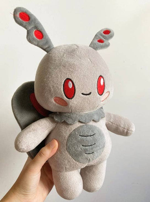 A hand holding a plush toy resembling a cute, gray mothman with red eyes and a happy expression.