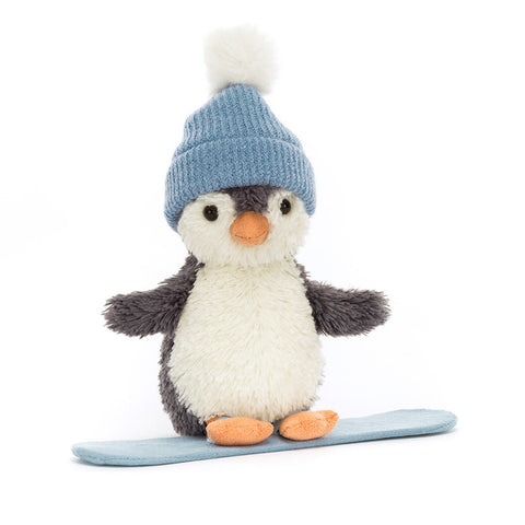 Stuffed penguin toy wearing a blue knitted hat and standing on a snowboard on a white background