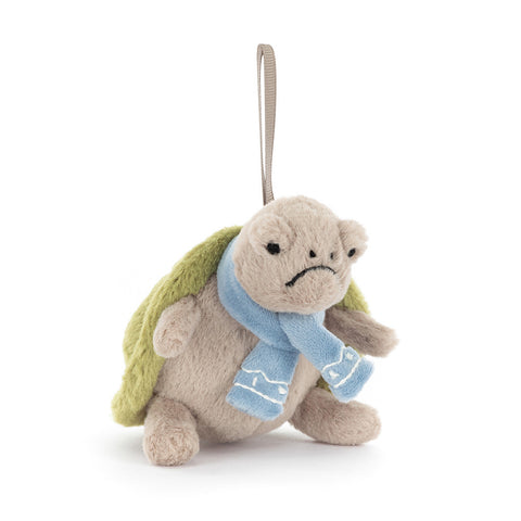 Plush turtle toy with a blue scarf on a white background. It hangs from a beige ribbon.