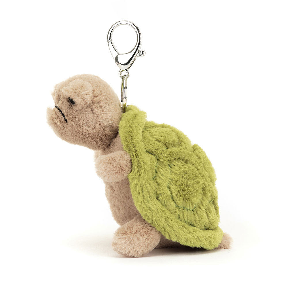 The side view of A stuffed turtle with a frowny face hanging from a clip keychain