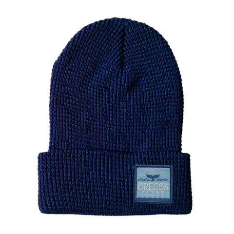 Image shows a navy blue waffle beanie. It has a small patch that reads "The Oregon Coast" and has a whale tail in the middle.