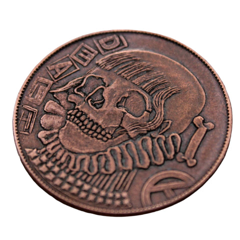 Copper coin with a skull and bones design on a textured surface. It says "Death"