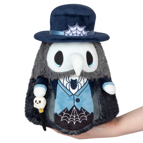 A plush toy depicting a mini haunted plague doctor with a blue hat, black coat, and holding a skull staff. His hat and shirt have spiderwebs.
