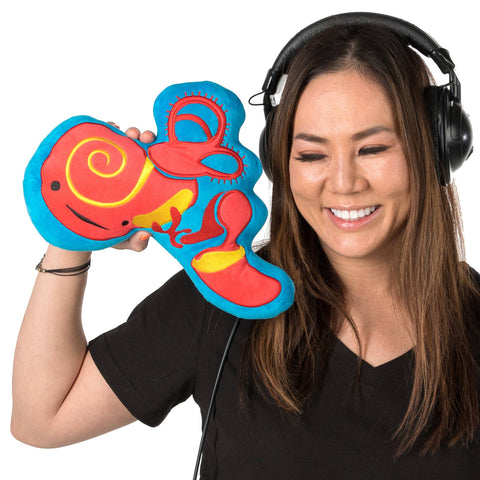 Image shows a woman wearing headphones holding the stuffed inner ear up to her face. It is slightly larger than her head.