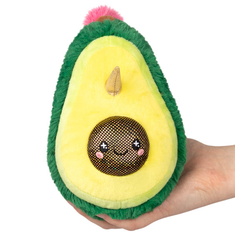 A hand holding a green and yellow stuffed toy resembling an avocado with a unicorn face and pink details.