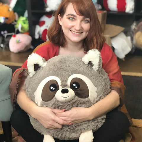 A woman holds the plush baby racoon in her lap. It is about the size of her torso.