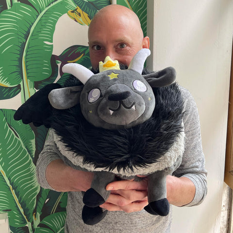 A man holds the plush Baphomet. It is about the size of his torso.