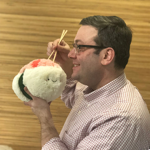 A man pretends to eat the plush shrimp sushi with chopsticks. It is approximately the size of his head.