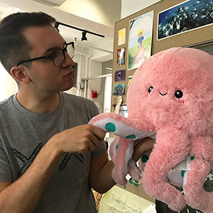 A man holds the plush ink octopus. It is about the size of his torso.