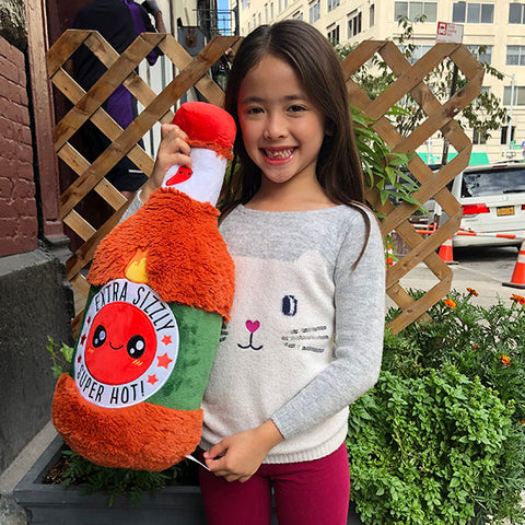 A child holds the plush hot sauce bottle. It is slightly larger than her torso.