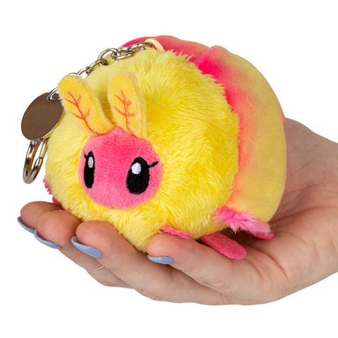 A plush yellow and pink rosy maple moth attached to a silver keychain clip held in someone's hand