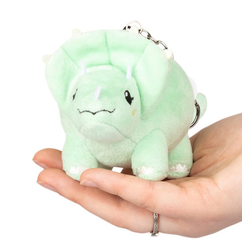 A small green plush toy resembling a Triceratops with a keychain attachment, being held in a person's hand.