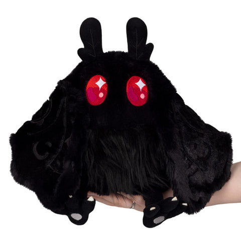 A plush toy resembling a shadowy, moth-like creature with red eyes, designed in a style reminiscent of the Mothman figure.