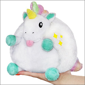 A hand holds a round plush unicorn. It has teal ears and hooves, and a rainbow mane and tail.