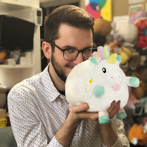 A man holds the plush baby unicorn up to his face. It is slightly larger than his head.