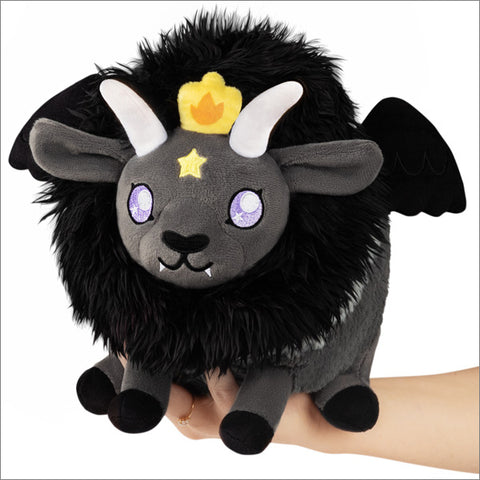 A plush toy resembling a black goat with bat wings, featuring a crown with a yellow star on the head, and purple glowing eyes. It is a Baphomet.