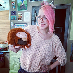 A woman holds the plush bigfoot. It is slightly larger than her head.