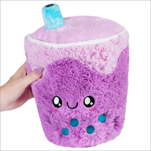 A plush toy designed to look like a purple bubble tea with a smiling face and bubble accents held in someone's hand