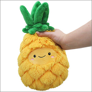 A hand holds a plush pineapple with a happy face