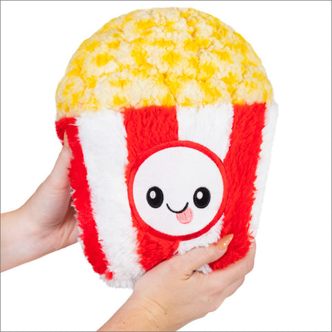 Two hands hold a plush popcorn toy in a red and white tub with a funny face