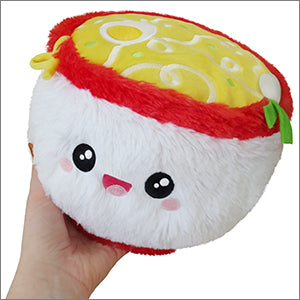 A hand holding a small, plush ramen toy with a red and yellow color scheme, designed to resemble a bowl of ramen noodles with a face on the side.