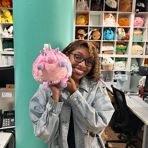 A woman holds the plush unicorn up to her face. It is slightly larger than her head.