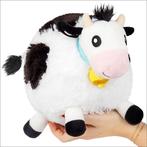 A plush cow with a round body, wearing a jingle bell.