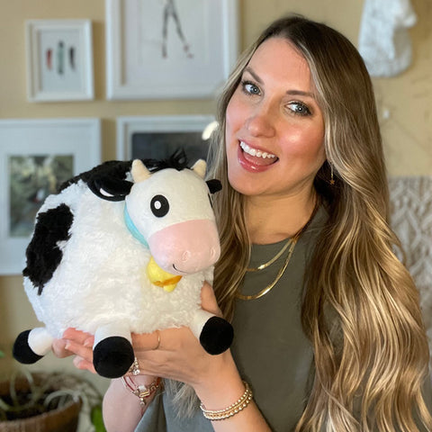 A woman holds the plush cow. It is slightly larger than her head.