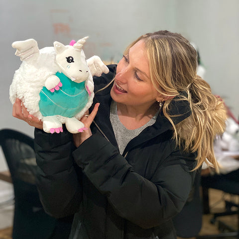 A woman holds the plush dragon. It is slightly larger than her head.