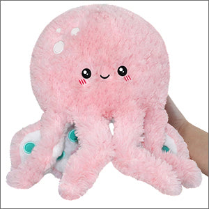 A small pink plush toy designed to resemble an octopus with a happy facial expression, held in a person's hand.