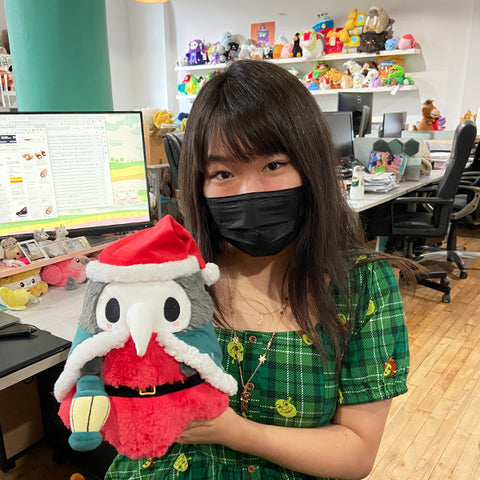 A woman wearing a mask holds the plush Festive Plague Doctor. It is slightly larger than her head.