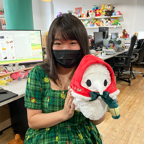 A woman holds the plush festive plague nurse near her face. It is slightly larger than her head.