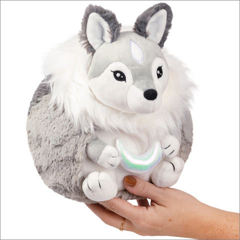 A plush wolflike creature with a white mane, holding a plush moon held in someone's hand